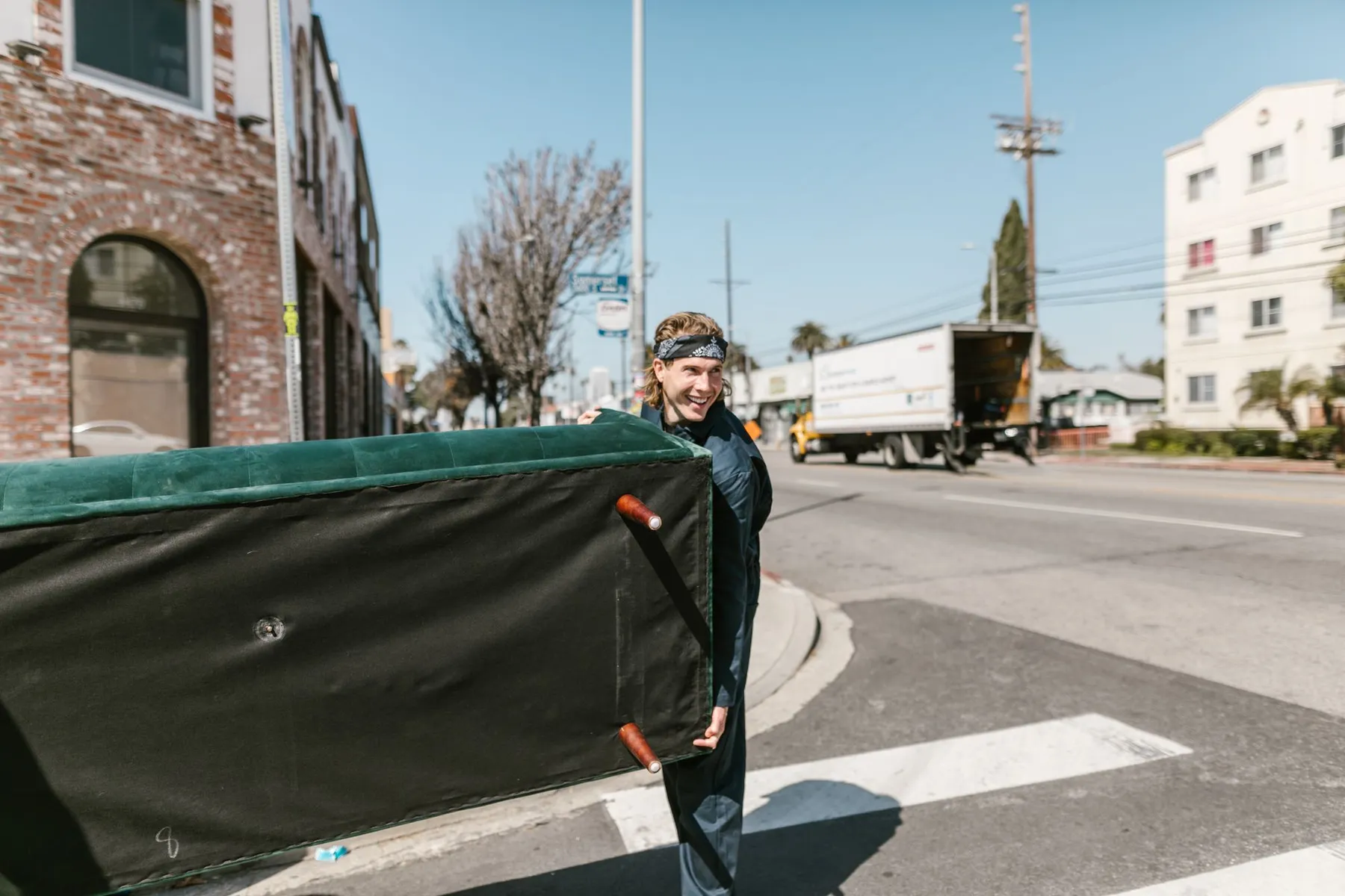 Mover carrying a large couch across a sunny city street