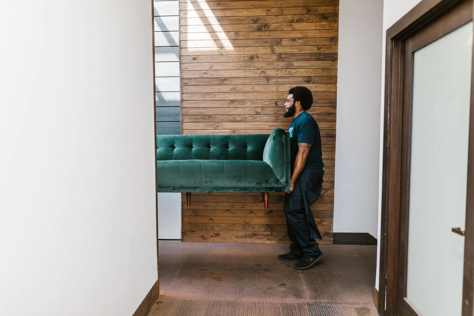 Mover carrying a green velvet sofa through a hallway