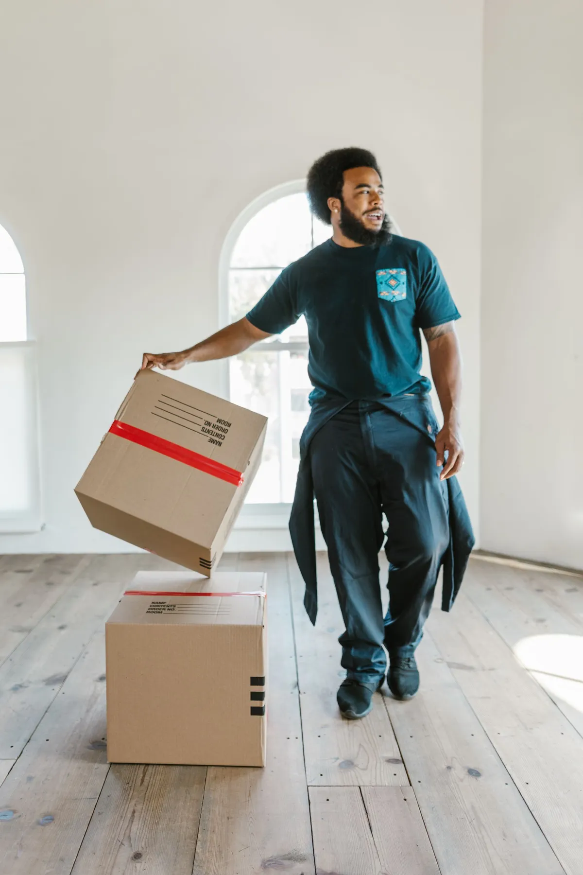 Mover tilting a taped moving box in a bright empty room