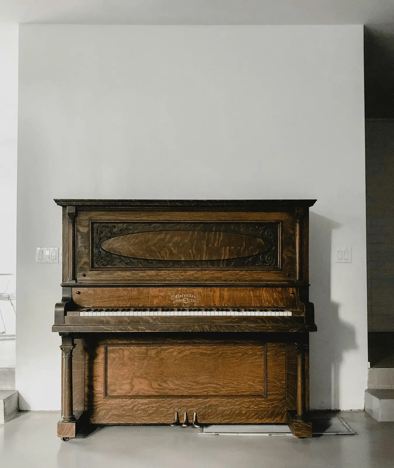 Antique wooden upright piano standing against a white wall